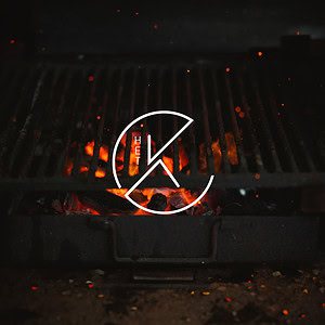 Een close-up van een barbecue met gloeiende rode kolen onder een donker metalen rooster, bedekt met een wit rond logo met de letter 'k', gescheiden door een diagonale lijn.