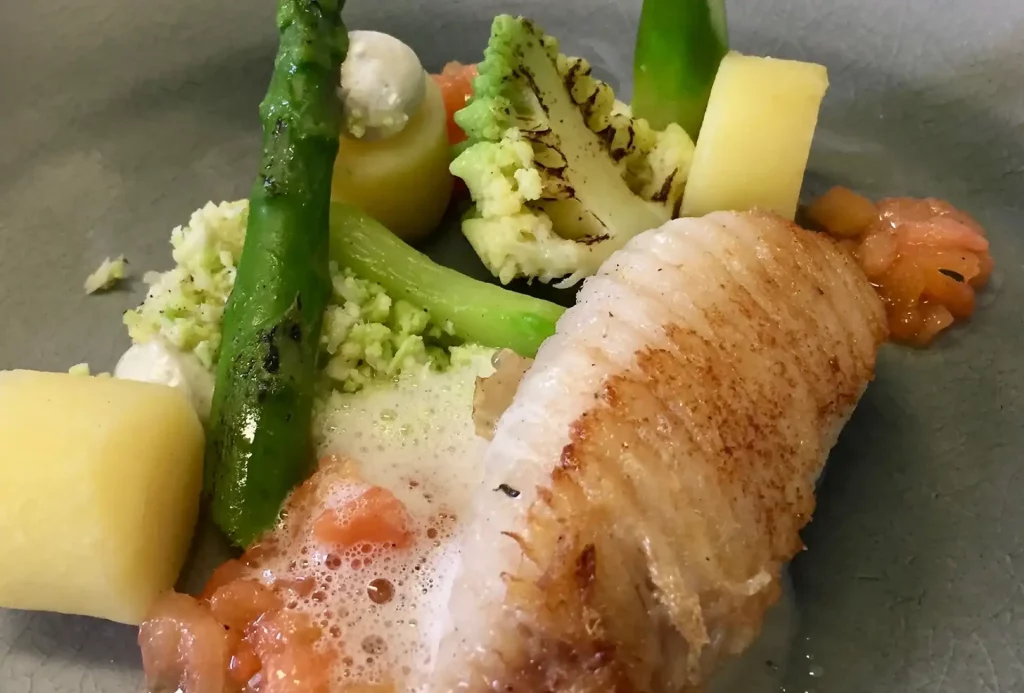 Gastronomisch bord met aangebraden visfilet, zalmkuit, diverse groene groenten zoals asperges en bloemkool en aardappelblokjes, artistiek gearrangeerd met een scheutje saus voor privé-evenementen.