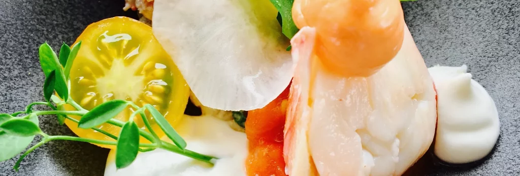 Een elegant gastronomisch gerecht, perfect voor privéfeesten, met verse garnalen, kleurrijke erfgoedtomaten, delicate groenten en klodders romige saus, kunstig gerangschikt op een leistenen serveerbord